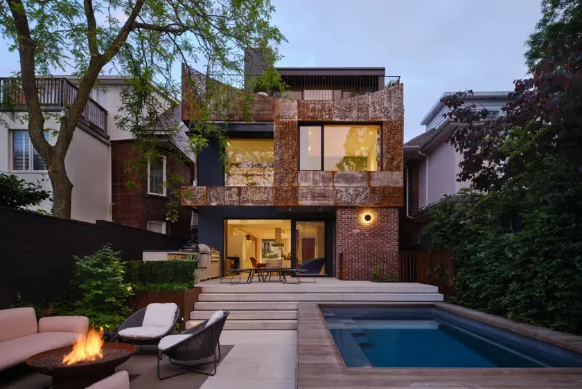 The exterior facade of a residential home features a sculptural weathering steel screen, a seating area to the left with a fire pit, and to the right, a small swim spa.