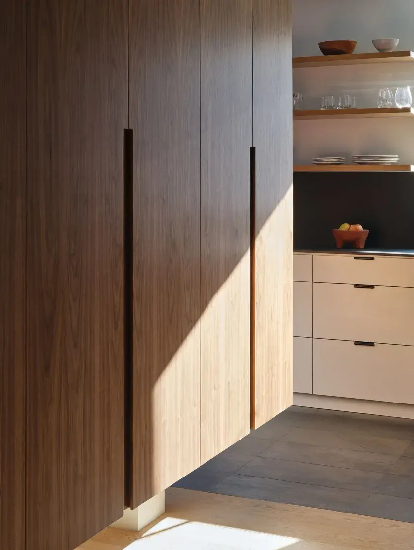 A close up of a walnut storage cabinet, slightly lit with sun streams, and a kitchen counter in the background